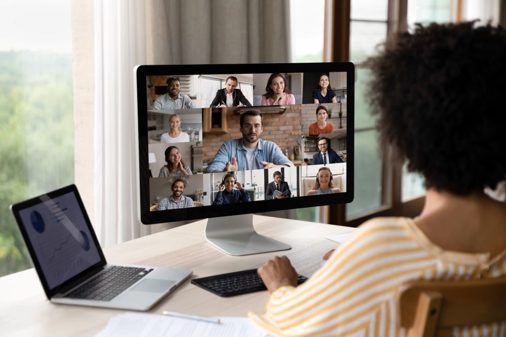 Professional joins a team video conference at a desk with charts displayed on a nearby laptop.