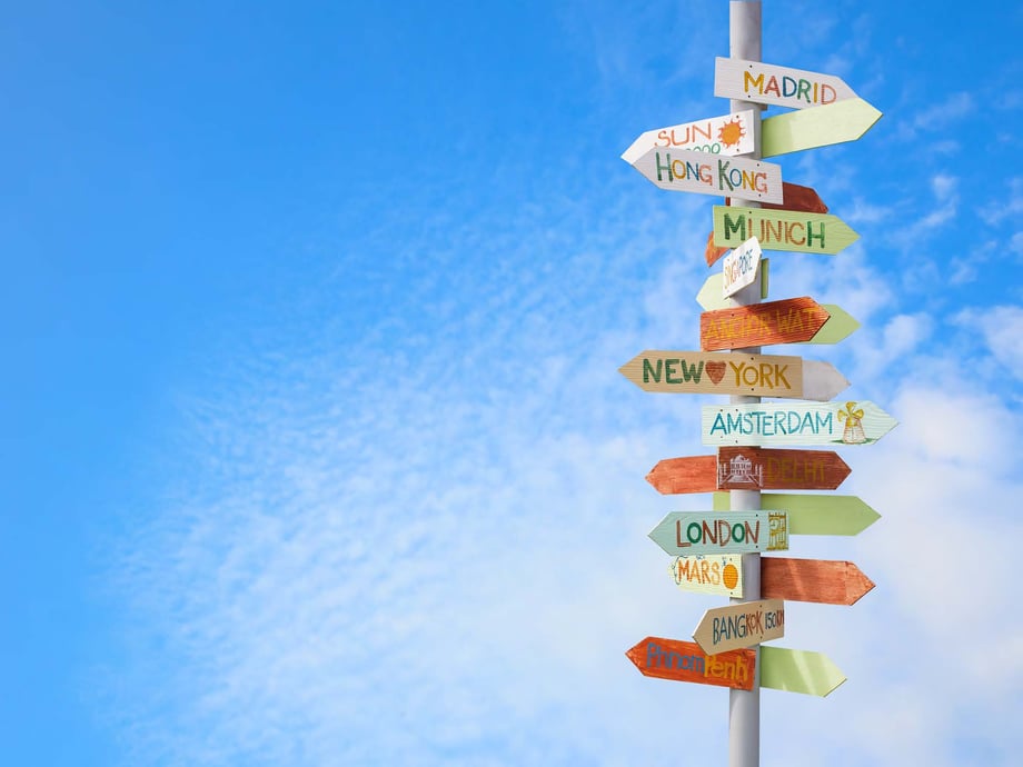 Colorful signpost with county signs pointing in different directions against clear blue sky - a metaphor for seamlessly transitioning to a new global mobility tax provider